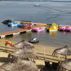 Słoneczna plaża Skorochów z parasolami, leżakami i kolorowymi łódkami wodnymi przy drewnianym pomoście.