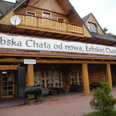 Drewniana Łebska Chata z banerem zapraszającym na odnowę. Obok grill i wolne pokoje.