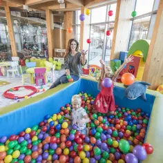 Wesoły hotel z salą zabaw dla dzieci. Dzieci bawią się w basenie z kulkami, a mama rzuca balonami.