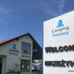 Witamy w Camping Portowy Mrzeżyno! Budynek recepcji i duży znak zapraszają na wypoczynek nad morzem.