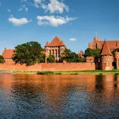 Potężny zamek w Malborku odbija się w wodzie. Zastanawiasz się, ile trwa zwiedzanie zamku w Malborku? Warto zaplanować cały dzień!