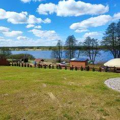Piękny dzień nad jeziorem skarlińskim. Błękitne niebo z białymi chmurami, zielona trawa i spokojna tafla wody.