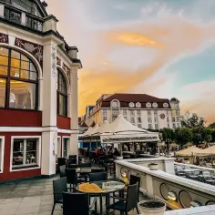 Wieczór w Trójmieście: taras restauracji z widokiem na zabytkową architekturę i zachodzące słońce. Idealne miejsce na romantyczne kolacje i wieczorne spotkania.