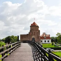 Drewniany most prowadzi do ceglanego zamku z czerwoną wieżą. To jedne z **ciekawe miejsca 150 km od Warszawy**.