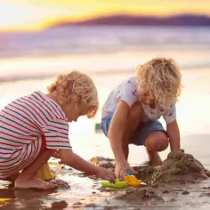 Dwóch chłopców buduje zamek z piasku na plaży podczas zachodu słońca. To nietypowe atrakcje dla dzieci, które zapewniają mnóstwo radości.