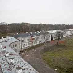 Długie, zabytkowe budynki Twierdzy Modlin zachęcają do zwiedzania. Widać liczne kominy na dachach i jesienne drzewa w tle.