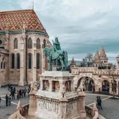 Budapeszt stare miasto: Rycerz na koniu przed kościołem z kolorowym dachem i basztami. Turyści spacerują po brukowanym placu.