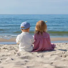 Dwoje dzieci siedzi na plaży, patrząc na morze. Idealne miejsce, gdzie z dzieckiem na weekend.