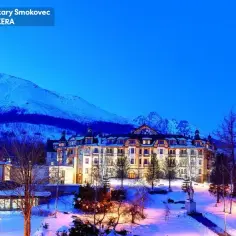Grandhotel Stary Smokovec w zimowej scenerii, oświetlony wieczorem, z ośnieżonymi górami w tle.