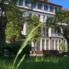 Sanatorium uzdrowiskowe Kołobrzeg-Podczele NFZ, otoczone zielenią, z ławkami w trawie.