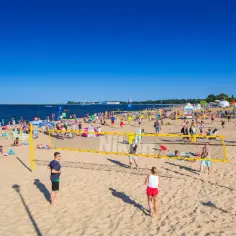 Słoneczna plaża Brzeźno tętni życiem. Ludzie grają w siatkówkę plażową, opalają się i spacerują.