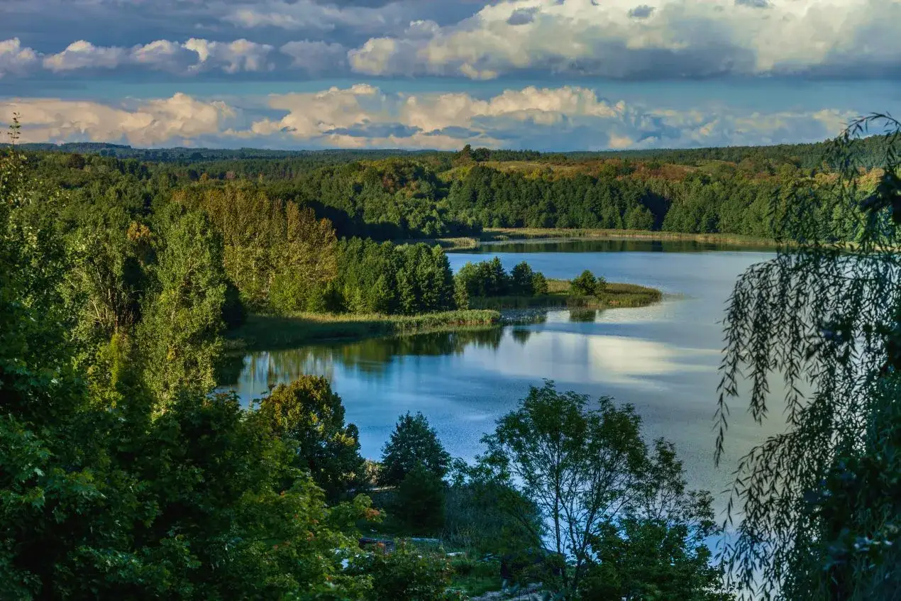 Malownicze jezioro skarlińskie otoczone zielonymi lasami, z pofalowanymi chmurami na niebie.