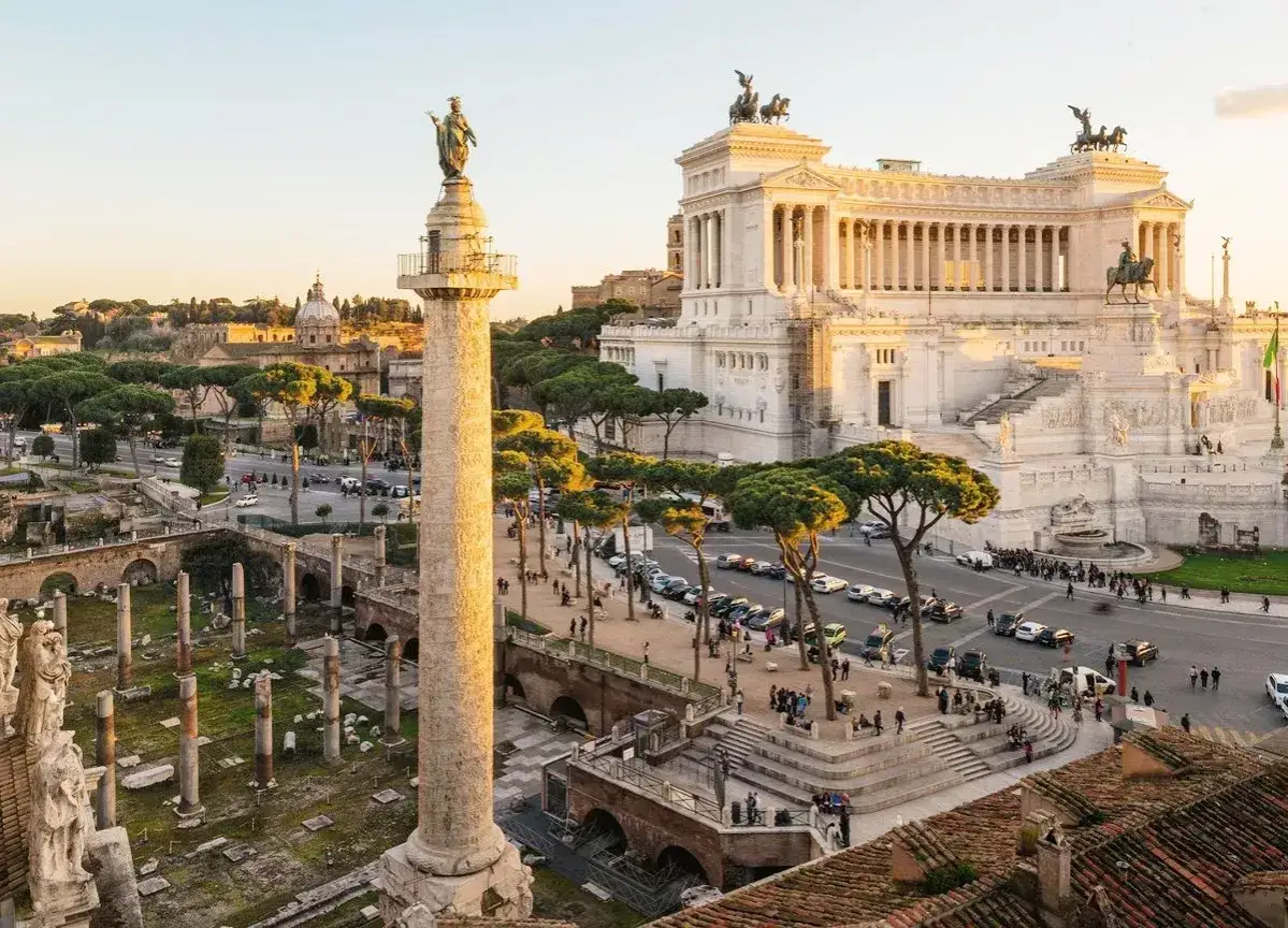 Zachód słońca nad Forum Romanum podczas zwiedzania Rzymu. Kolumna Trajana i Ołtarz Ojczyzny w złotej poświacie.