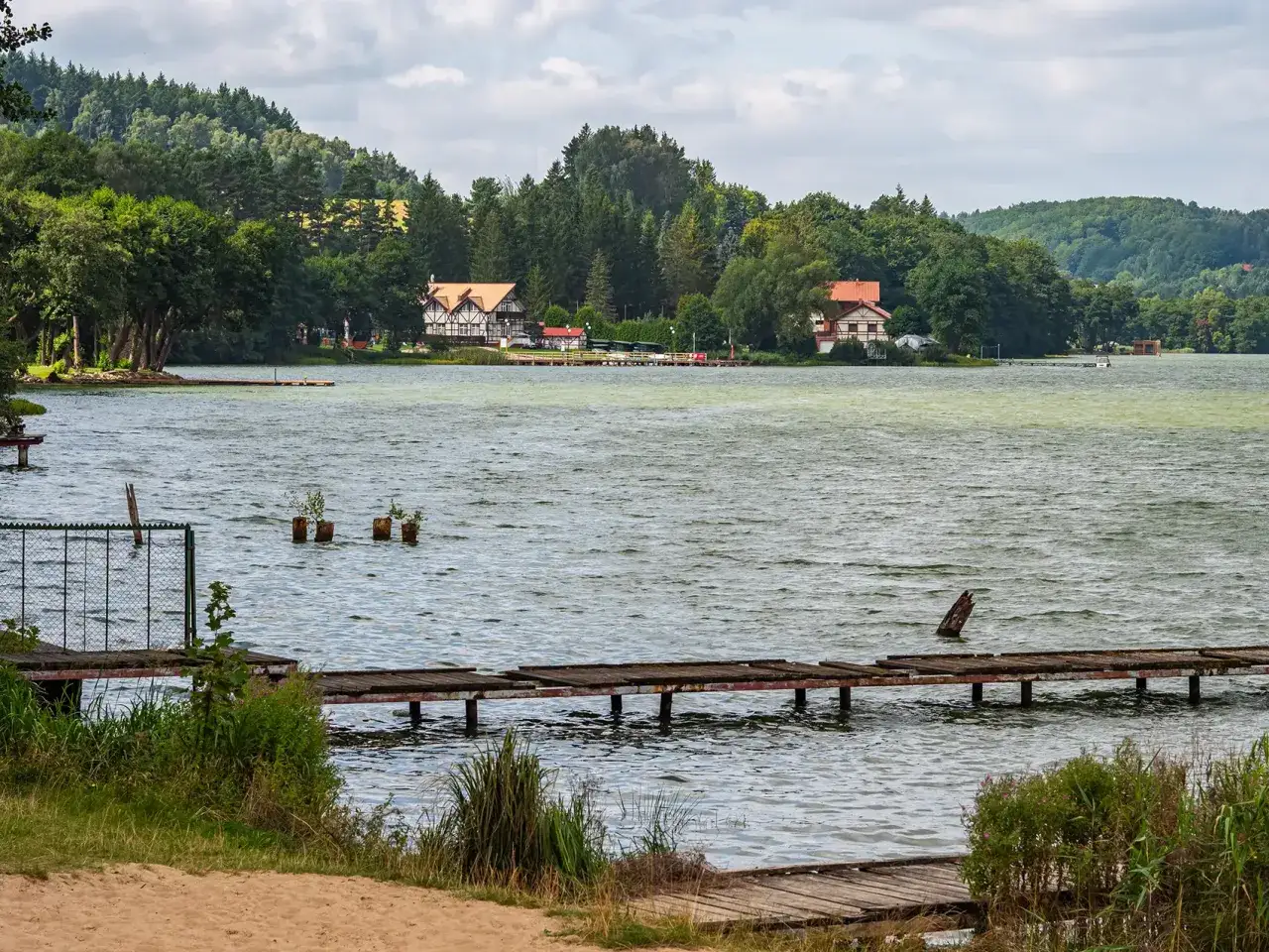 Piękne jezioro na Kaszubach, idealne do zwiedzania samochodem. Dwa domy z czerwonymi dachami na tle zielonych wzgórz.