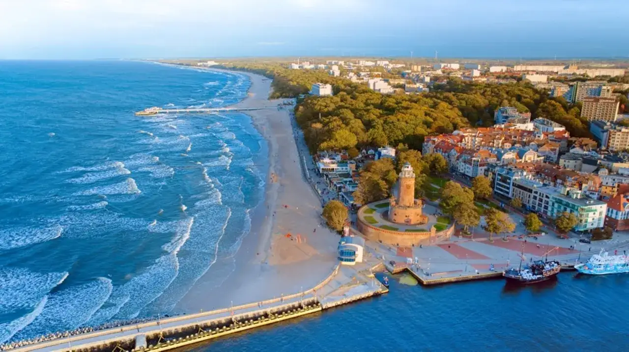 Widok na Kołobrzeg z latarnią morską, plażą i morzem. Ciekawe, ile mieszkańców ma Kołobrzeg, bo miasto wygląda na tętniące życiem.
