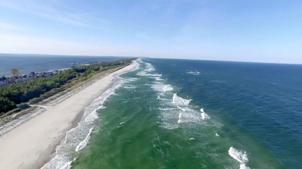 Szeroka plaża i zielone morze, gdzie kitesurferzy ścigają się w okolicach portu na Helu.