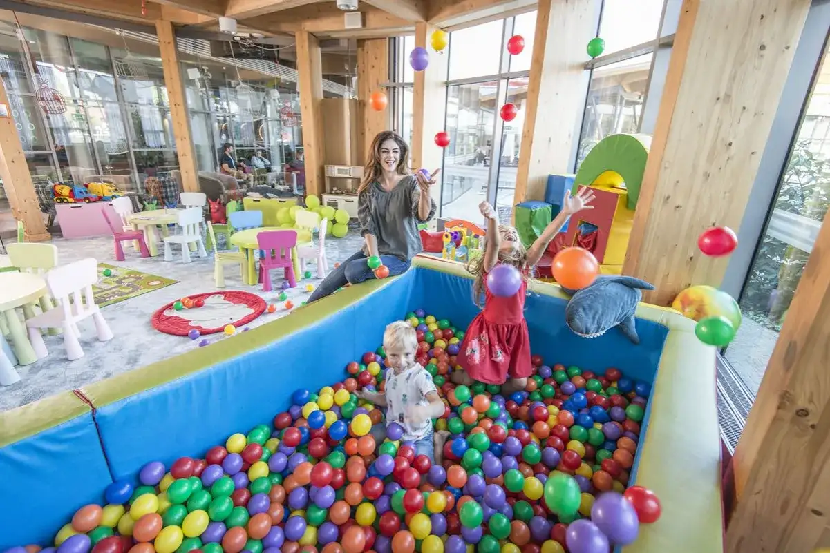 Wesoły hotel z salą zabaw dla dzieci. Dzieci bawią się w basenie z kulkami, a mama rzuca balonami.