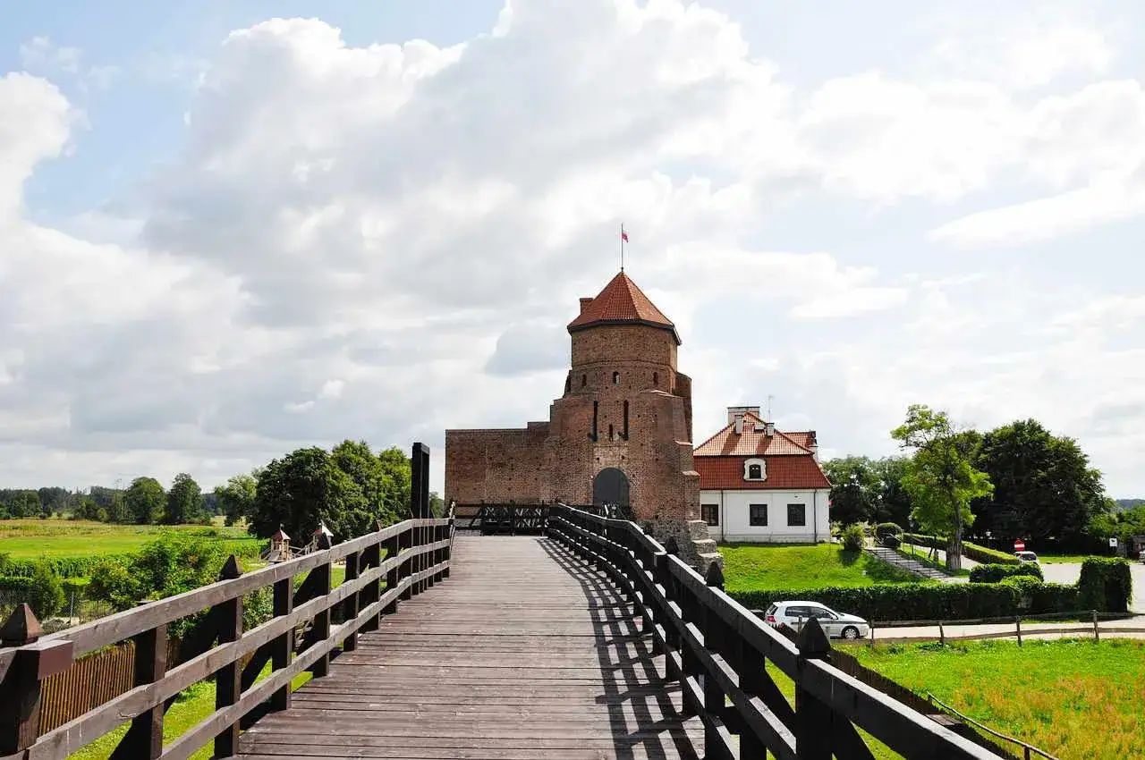 Drewniany most prowadzi do ceglanego zamku z czerwoną wieżą. Idealne ciekawe miejsca 150 km od Warszawy na weekendową wycieczkę.
