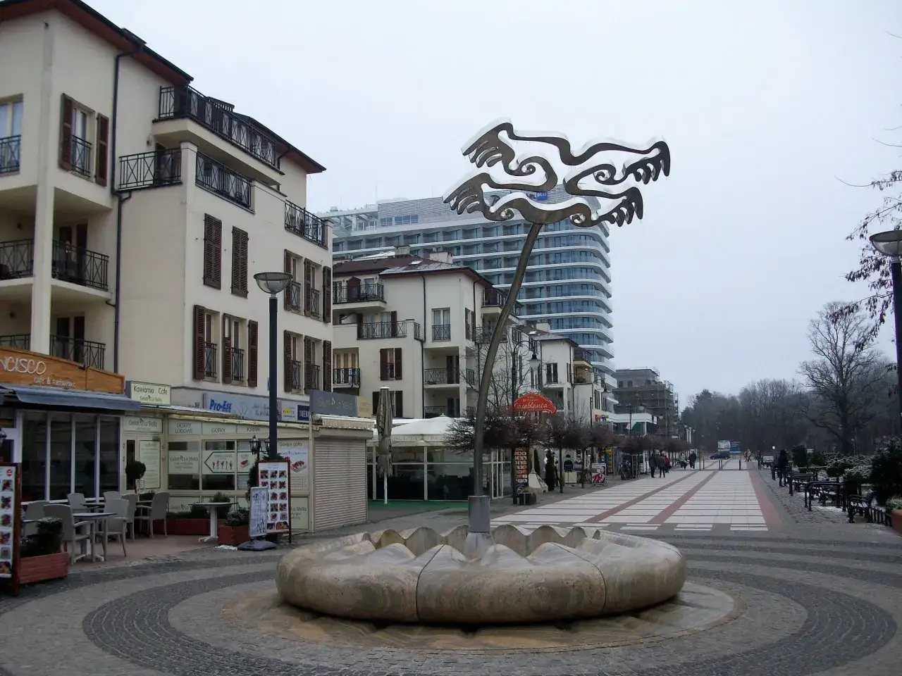 Kamienna fontanna i nowoczesna rzeźba na tle kamienic i hotelu w Świnoujściu, stare miasto.