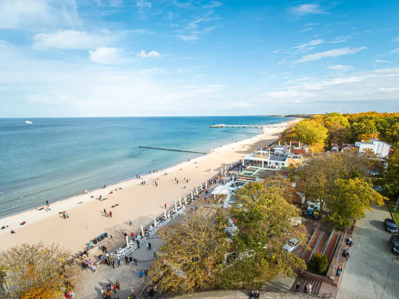 Piękna plaża i morze, idealne miejsce, by zastanowić się, gdzie na wakacje. Widać ludzi spacerujących i odpoczywających.