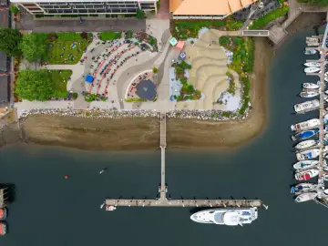 Widok z lotu ptaka na ruchliwy **Olimpia Port** z ludźmi siedzącymi na trawie i łodziami przycumowanymi do nabrzeża.