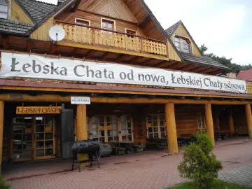 Drewniana Łebska Chata z banerem zapraszającym na odnowę. Obok grill i wolne pokoje.