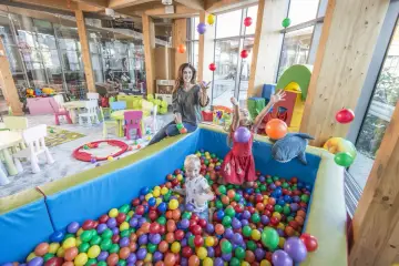 Wesoły hotel z salą zabaw dla dzieci. Dzieci bawią się w basenie z kulkami, a mama rzuca balonami.