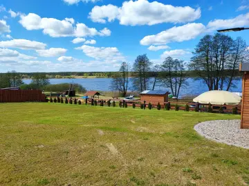 Piękny dzień nad jeziorem skarlińskim. Błękitne niebo z białymi chmurami, zielona trawa i spokojna tafla wody.