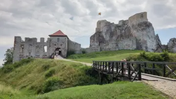 Kamienny zamek w Olkuszu, z mostkiem i zielonymi wzgórzami.