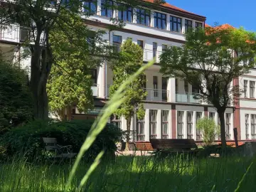 Sanatorium uzdrowiskowe Kołobrzeg-Podczele NFZ, otoczone zielenią, z ławkami w trawie.