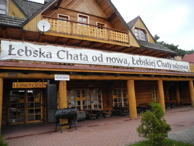 Drewniana Łebska Chata z banerem zapraszającym na odnowę. Obok grill i wolne pokoje.