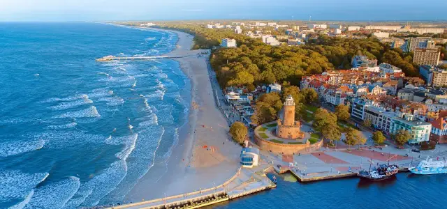 Widok na port w Kołobrzegu z latarnią morską, plażą i morzem.