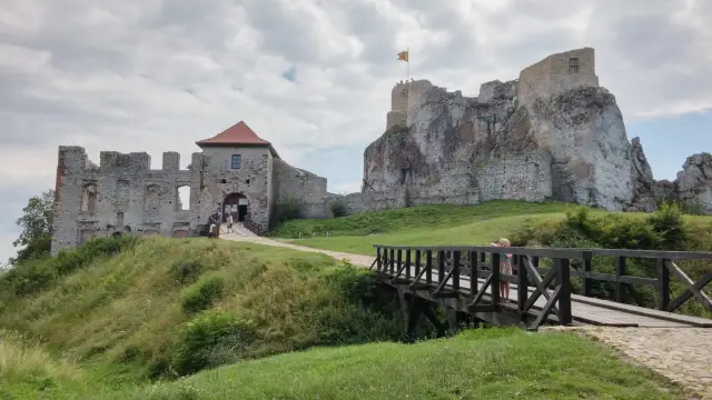 Kamienny zamek w Olkuszu, z mostkiem i zielonymi wzgórzami.
