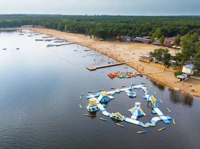 Sielpia jezioro tętni życiem. Na piaszczystej plaży wypoczywają ludzie, a w wodzie szaleją na dmuchanym torze przeszkód.