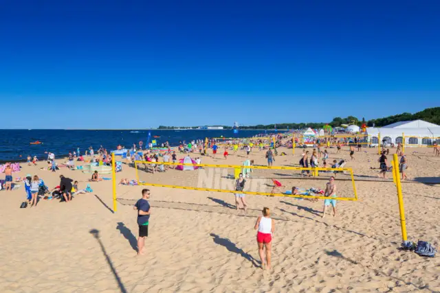 Słoneczna plaża Brzeźno tętni życiem. Ludzie grają w siatkówkę plażową, opalają się i spacerują.